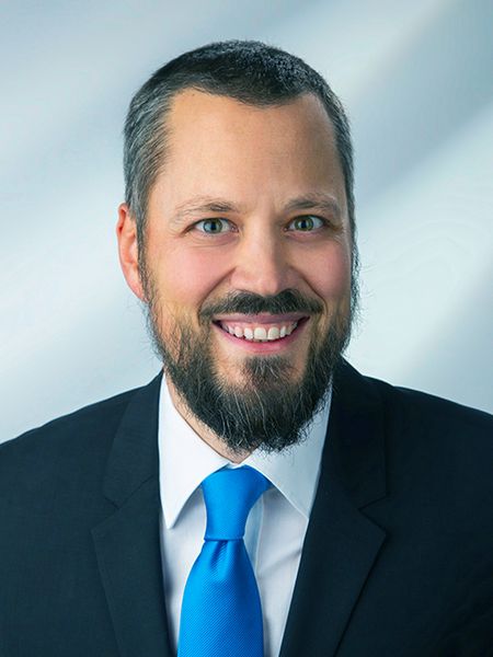 Porträt von Florian Parnigoni im dunklen Anzug mit weißem Hemd und blauer Krawatte