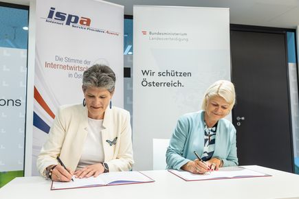 ISPA-Vize-Präsidentin Natalie Ségur-Cabanac (links) und Verteidigungsministerin Klaudia Tanner (rechts) sitzen an einem Tisch und unterzeichnen die Kooperationsvereinbarung der ISPA und des Österreichischen Bundesheeres.