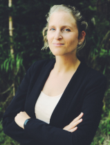 Portrait von Charlotte Steenbergen. Sie tr&auml;gt ein wei&szlig;es Oberteil unter einen shwarnzen Bl&auml;ser, ihre Arme sind vor der Brust verschr&auml;nkt. Sie schaut freundlich in die Kamera.