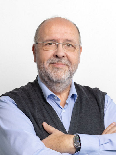 Portrait Peter Miller: Er tr&auml;gt ein blaues Hemd, dar&uuml;ber eine graue Weste. Er l&auml;chelt mit geschlossenem Mund und blickt direkt in die Kamera. Seine Arme sind vor der Brust verschr&auml;nkt.