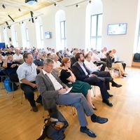 Zahlreiche G&auml;ste interessierten sich f&uuml;r die Blockchain. Das Publikum ist von schr&auml;g vorne abgebildet. Der Saal ist sehr gut gef&uuml;llt, alle sehen interessiert Richtung Podium.