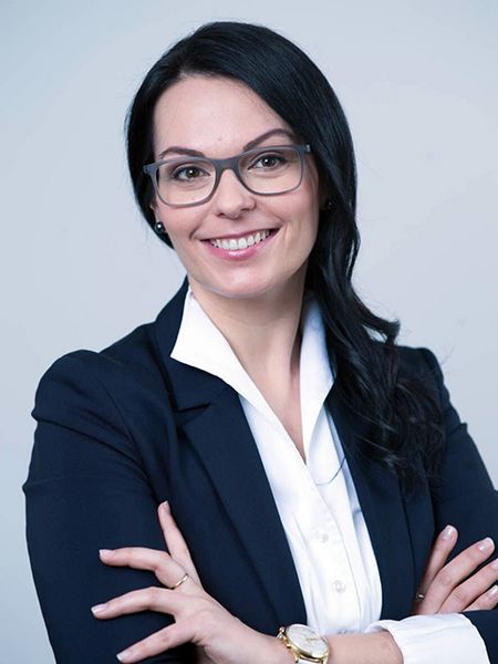 ISPA Vorstand Monika Valcanover Porträt von Monika Valcanover mit vor der Brust verschränkten Armen, sie trägt einen dunkelblauen Blazer über einer weißen Bluse. Sie lächelt mit geöffneten Mund und trägt eine große, dunkle Brille.