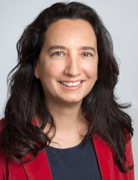 Anita Thaler Anita Thaler, mit langen, dunklen Haaren trägt ein graues Oberteil und einen roten Blazer, freundlich lächeln und die Zähne sind sichtbar